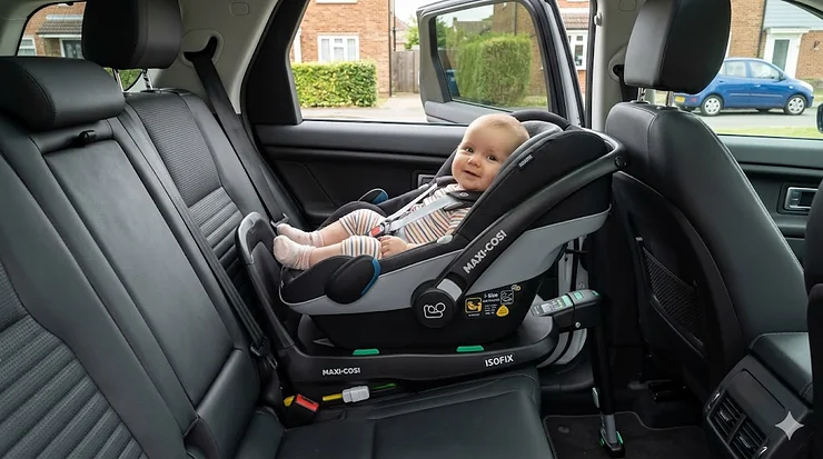 A photorealistic view of a baby resting in a rear-facing i-size car seat installed in the back of a UK family car. i-size car seat