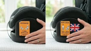 A photorealistic close-up photograph comparing the ECE R44/04 orange approval label and the newer R129 (i-Size) standard labels on the side of the car seat.