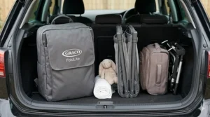 A folded compact travel cot packed neatly into the boot of a British family car alongside holiday luggage.