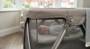 Parent assembling a portable travel cot with bassinet in a nursery.