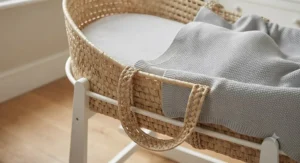 Close-up of a natural wicker moses basket set featuring a soft mattress and a grey knitted blanket.