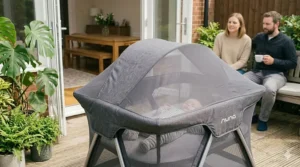 A pop-up travel cot featuring an integrated sun shade for outdoor or holiday use.