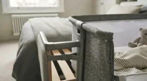 Close-up of a bedside crib securely attached to an adult bed frame for safe co-sleeping.