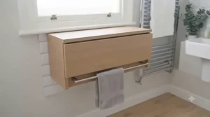 Foldable changing table closed flat against the bathroom wall to function as a discreet storage shelf when not in use.