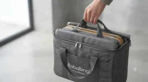 The folded travel changing table packed neatly inside its matching waterproof carry bag with a shoulder strap.