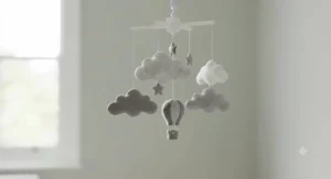 A decorative, photorealistic nursery mobile featuring soft felt clouds and a small hot air balloon hanging above a cot.